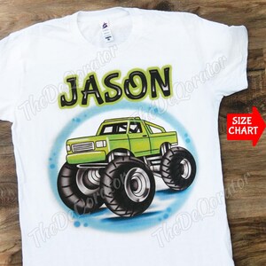 Puede incluir: Camiseta blanca con un camión monstruo verde aerografiado en la parte delantera. El camión tiene grandes neumáticos negros y el nombre "JASON" está escrito encima.