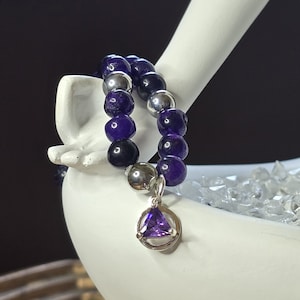 May include: A double-strand bracelet with purple and silver beads, featuring a silver pendant with a purple triangular gemstone.