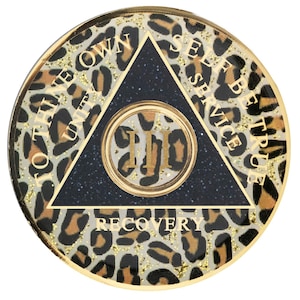 May include: A gold-colored round coin with a black triangle in the center. The triangle has the words "To thine own self be true" on the top, "Unity" on the left, "Service" on the right, and "Recovery" on the bottom. The center of the triangle has a smaller circle with the letters "III" inside. The coin has a leopard print pattern.