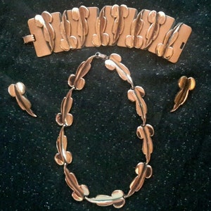 May include: A gold-toned jewelry set with a necklace, bracelet, and earrings. The pieces are made of linked, stylized leaf shapes.