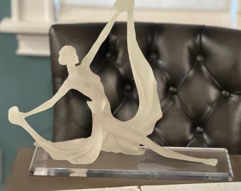 May include: A white, translucent sculpture of a woman in a flowing dress. The sculpture is on a clear acrylic base.