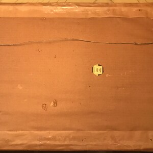 May include: The back of a framed picture with a brown cardboard backing. A small yellow label is attached to the cardboard. The label has text that is too small to read.