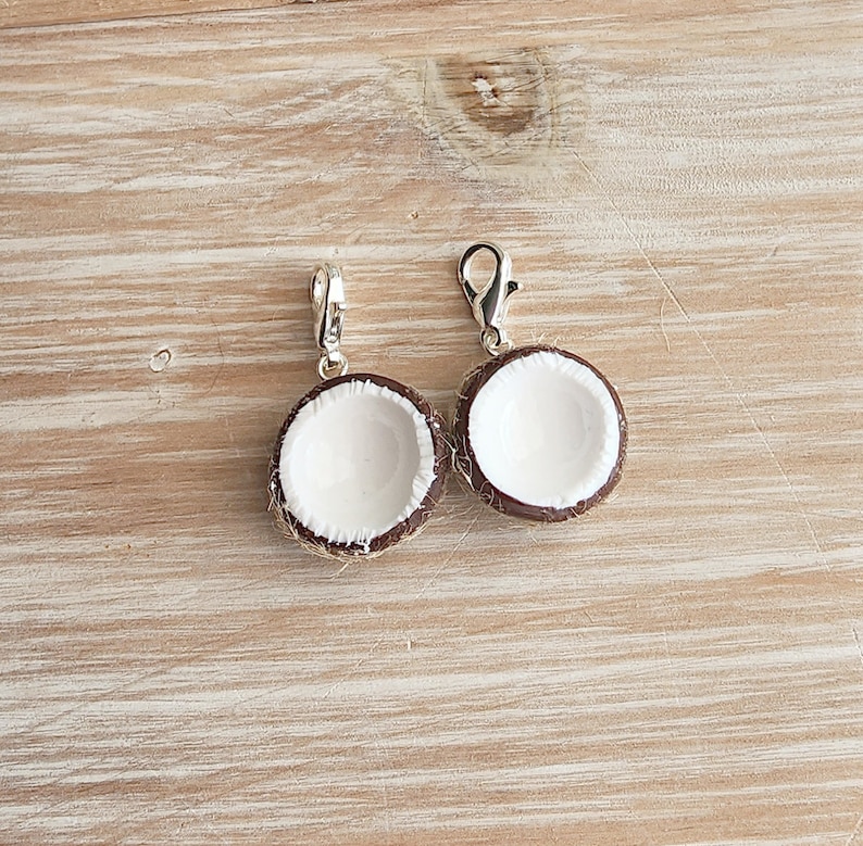 May include: Two silver charm pendants shaped like halved coconuts with brown outsides and white insides. The charms are hanging from silver jump rings.