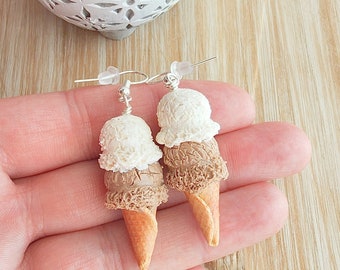 May include: A pair of dangle earrings featuring miniature ice cream cones with three scoops of ice cream. The ice cream is white and brown, and the cones are a light brown color.