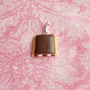 May include: A chocolate-covered cookie charm with a silver clasp. The cookie is light brown with a dark brown chocolate topping and a white filling.