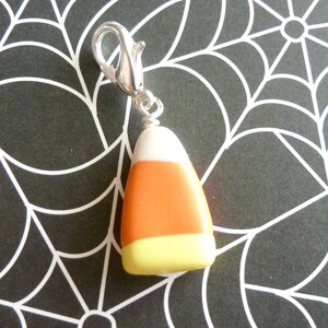 May include: A silver charm in the shape of a candy corn. The candy corn is white, orange, and yellow.