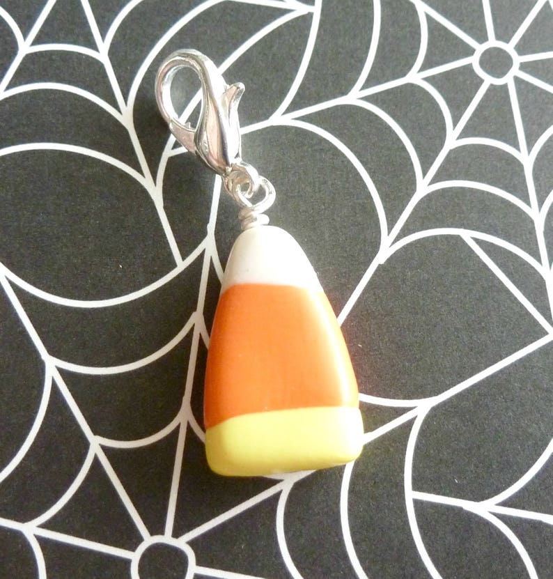 May include: A silver charm in the shape of a candy corn. The candy corn is white, orange, and yellow.