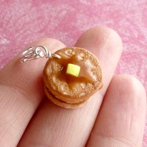 May include: A silver charm in the shape of a stack of two mini pancakes with a yellow pat of butter on top.