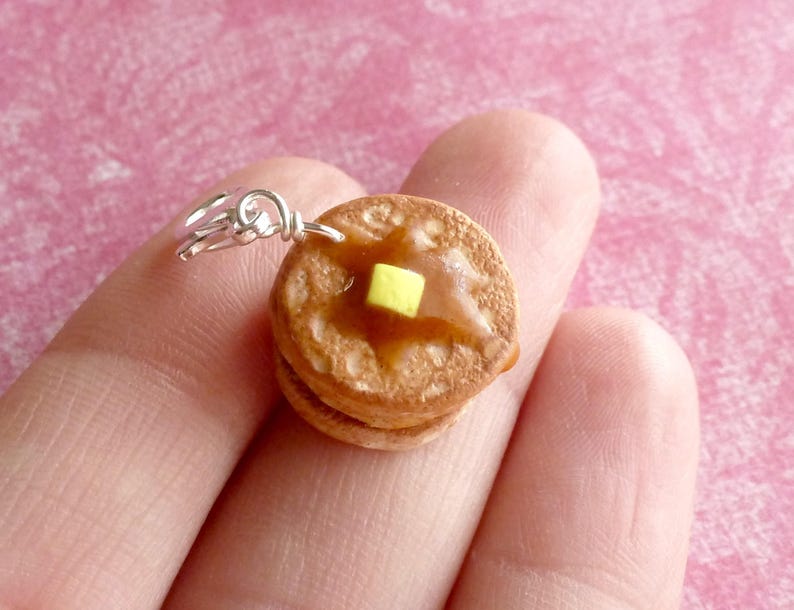 May include: A silver charm in the shape of a stack of two mini pancakes with a yellow pat of butter on top.