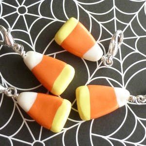 May include: Four candy corn charms with silver jump rings. The charms are made of polymer clay and are shaped like candy corn. The charms are orange, yellow, and white.