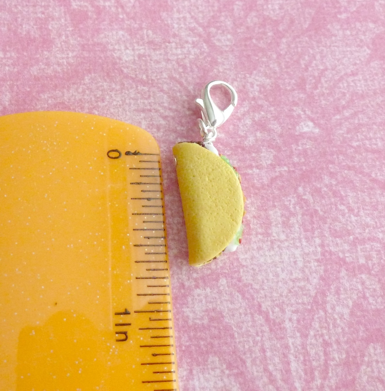 May include: A small, yellow taco charm with a silver clasp. The taco is filled with lettuce, tomato, and cheese.
