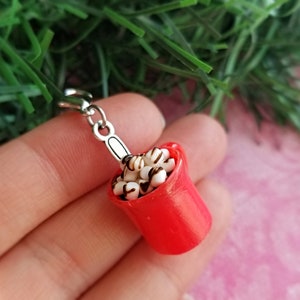 May include: A miniature red mug filled with white marshmallows drizzled with chocolate. The mug has a silver handle and is attached to a silver clasp. The charm is a festive accessory.