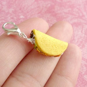 May include: A silver charm in the shape of a taco. The taco is filled with meat, cheese, and lettuce. The charm is attached to a silver clasp.