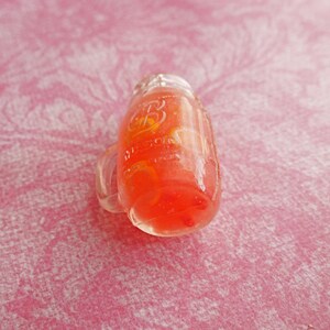 May include: A clear glass jar with a red liquid and a yellow citrus fruit inside. The jar has a handle and a label that reads "Ball."