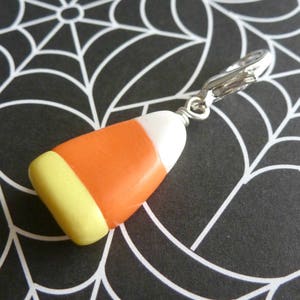 May include: A silver charm in the shape of a candy corn with orange, yellow, and white stripes. The charm is attached to a silver chain.
