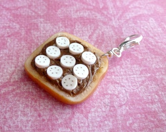 Peut inclure: Un charme en forme de toast avec du chocolat et des pépites de chocolat blanc, de couleur marron et blanche. Le charme est attaché à un fermoir en métal argenté.