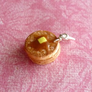 May include: A charm of a stack of two miniature pancakes with a yellow pat of butter on top. The charm is made of polymer clay and has a silver jump ring.