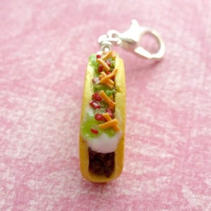 May include: A miniature polymer clay hot dog keychain with a yellow bun, white sauce, green lettuce, red ketchup, and orange cheese.