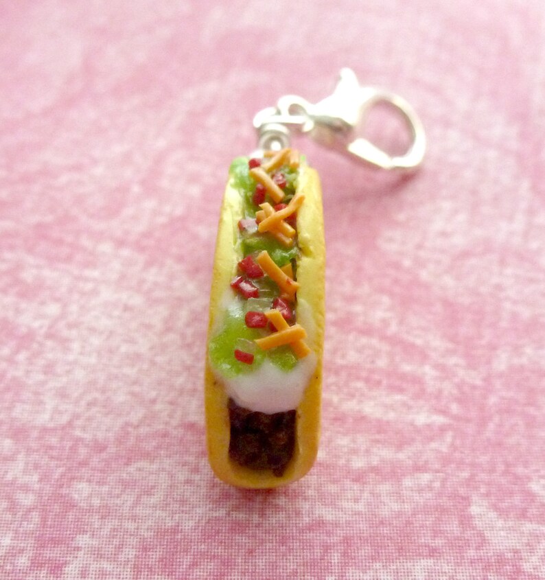 May include: A miniature polymer clay hot dog keychain with a yellow bun, white sauce, green lettuce, red ketchup, and orange cheese.
