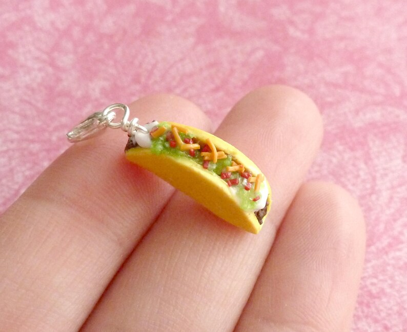 May include: A silver charm in the shape of a taco. The taco is filled with lettuce, cheese, and meat. The charm is perfect for adding a touch of fun to your jewelry.