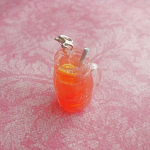 May include: A glass jar filled with a pink and orange drink with a straw and a silver lid. The jar is sitting on a pink surface.