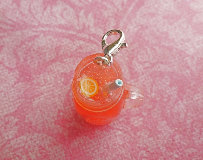May include: A red and orange plastic charm shaped like a mason jar with a straw and a lemon slice. The charm has a silver metal clasp.