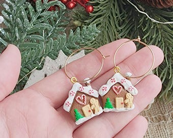May include: A pair of gold hoop earrings with gingerbread house charms. The charms are decorated with white icing, red candy canes, and green trees.