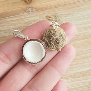 May include: Two miniature coconut shell charms with silver clasps. One coconut is whole and the other is split open to reveal the white inside.