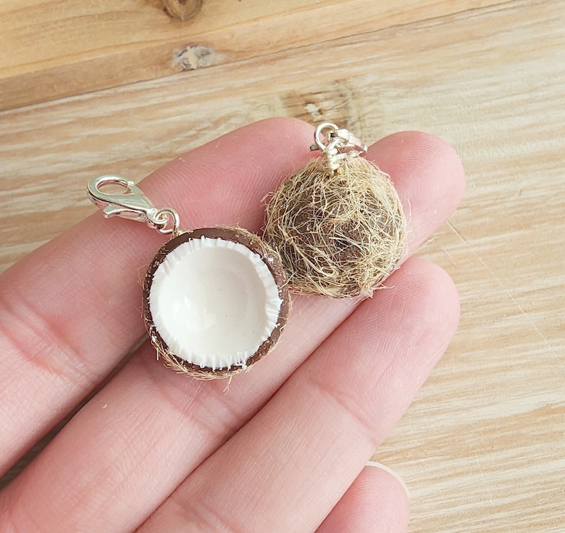 May include: Two miniature coconut shell charms with silver clasps. One coconut is whole and the other is split open to reveal the white inside.
