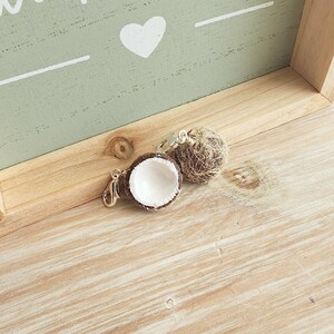 May include: Two small coconut shell charms with a silver clasp. One coconut shell is open and the other is closed with a brown husk.