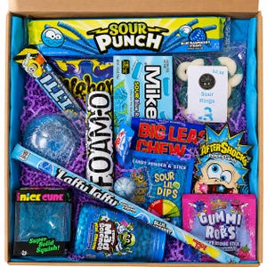 May include: A cardboard gift box filled with blue and purple crinkle paper containing various candies including Sour Punch Blue Raspberry Straws, Mike and Ike Sour Blue, a bag of sour rings, Big League Chew, Aftershocks, and Laffy Taffy.