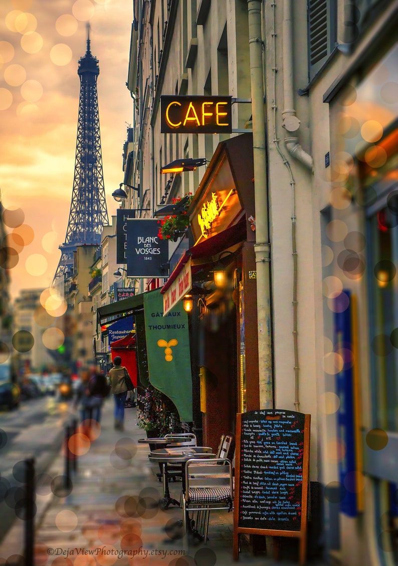 May include: A Parisian cafe with a cafe sign, a menu board, and tables and chairs set up outside. The Eiffel Tower is visible in the background.