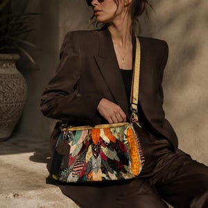 Könnte beinhalten: Bunte Patchwork-Umhängetasche mit verschiedenen Stoffen und Mustern. Die Tasche hat einen gelben Riemen und einen Reißverschluss. Die Person trägt einen braunen Anzug und eine Sonnenbrille.