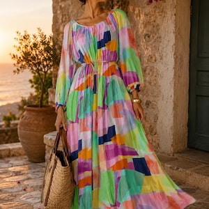Pu&ograve; includere: Un abito lungo e colorato con maniche lunghe e un motivo geometrico nei toni del rosa, verde, blu e giallo. L'abito &egrave; stretto in vita con una sottile cintura e abbinato a una borsa tote in paglia. Lo sfondo presenta un muro di pietra e un tramonto.