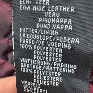 K&ouml;nnte beinhalten: Ein schwarzes Pflegeetikett mit wei&szlig;em Text zur Materialzusammensetzung. Es gibt Rindsleder, ein Futter und eine Wattierung aus 100 % Polyester sowie einen Webpelzbesatz aus 80 % Acryl und 20 % Polyester f&uuml;r das Kleidungsst&uuml;ck an.