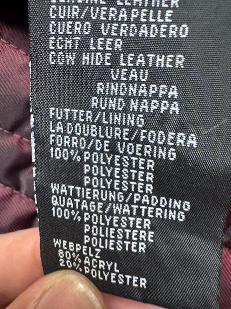 K&ouml;nnte beinhalten: Ein schwarzes Pflegeetikett mit wei&szlig;em Text zur Materialzusammensetzung. Es gibt Rindsleder, ein Futter und eine Wattierung aus 100 % Polyester sowie einen Webpelzbesatz aus 80 % Acryl und 20 % Polyester f&uuml;r das Kleidungsst&uuml;ck an.