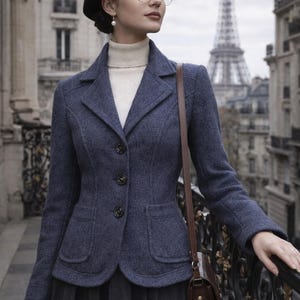 May include: A woman wearing a navy blue blazer, black beret, and round glasses, standing on a balcony with the Eiffel Tower in the background. The blazer has three dark buttons and two front pockets. She is also wearing a white turtleneck and a dark skirt.