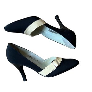May include: Black and beige high-heeled pumps. The shoes have a pointed toe and a strap across the top. The heels are approximately 3 inches tall. The brand name "Casadei" is visible on the insole.