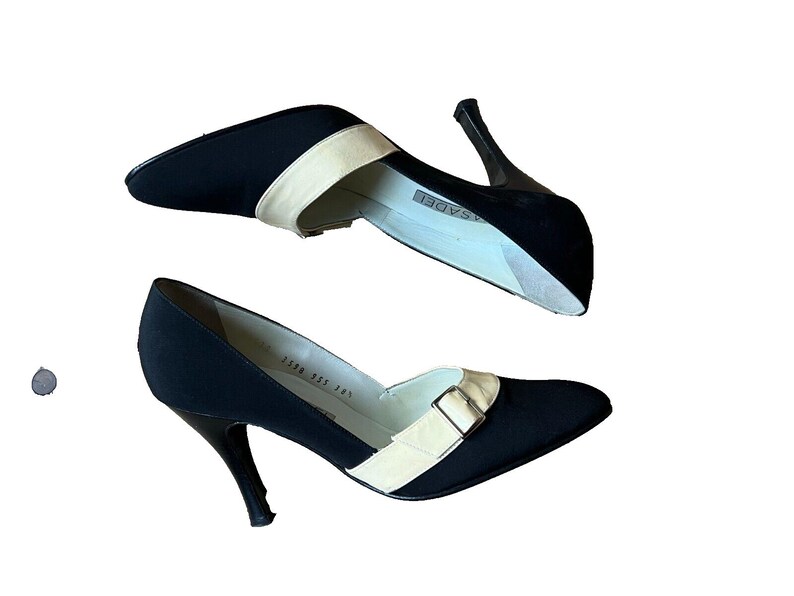 May include: Black and beige high-heeled pumps. The shoes have a pointed toe and a strap across the top. The heels are approximately 3 inches tall. The brand name "Casadei" is visible on the insole.