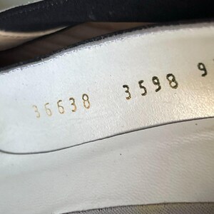 May include: Close-up of the inside of a white shoe. Gold numbers are stamped on the white leather, including "35638", "3598", and "955". The shoe's interior is visible, with a black lining at the top.