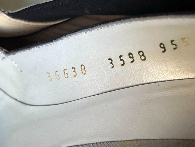 May include: Close-up of the inside of a white shoe. Gold numbers are stamped on the white leather, including "35638", "3598", and "955". The shoe's interior is visible, with a black lining at the top.