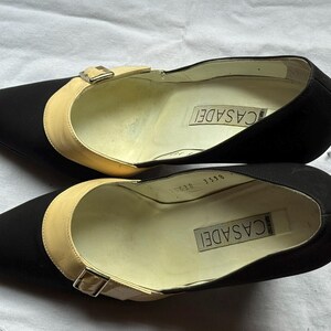 May include: A pair of black Casadei pumps with a pointed toe and a beige strap across the top, secured with a small buckle. The brand name is visible inside the shoe.