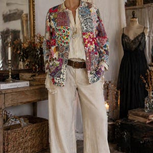 Könnte beinhalten: Eine Frau trägt eine bunte Patchwork-Jacke mit einer cremefarbenen Bluse und einer Hose mit weitem Bein. Die Jacke hat Blumen- und Paisley-Muster. Ein brauner Gürtel betont die Taille. Das Outfit hat einen Boho-Stil.