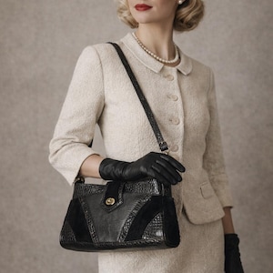 Könnte beinhalten: Ein cremefarbener Tweed-Anzug mit passendem Rock und Jacke. Die Frau trägt eine schwarze Handtasche mit strukturierter Vorderseite und schwarze Lederhandschuhe. Eine Perlenkette und Ohrringe vervollständigen den Look.
