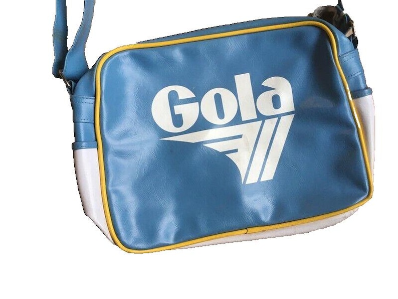 May include: A blue shoulder bag with the word "Gola" in white block letters. The bag has a white and yellow trim, and a blue shoulder strap. The bag is made of a synthetic material.