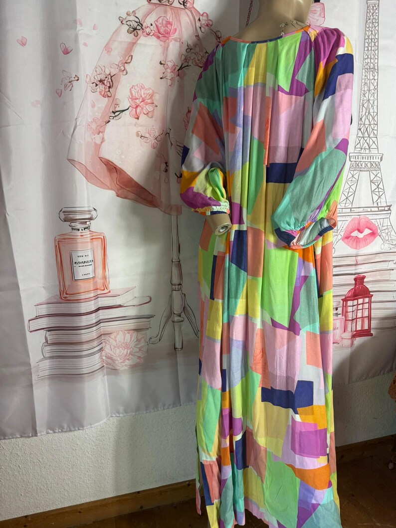 Pu&ograve; includere: Un abito lungo e fluido con un colorato motivo geometrico. L'abito presenta un mix di colori vivaci tra cui rosa, verde, giallo e blu. Ha maniche lunghe e scollatura rotonda. L'abito sembra essere realizzato in un tessuto leggero.