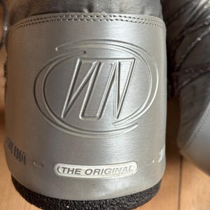 May include: Close-up of a gray winter boot with a silver logo and the text "THE ORIGINAL". The boot has a textured upper and a black sole. The logo is a stylized "WN" within a circle.