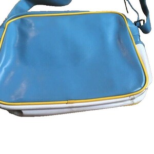 May include: A blue, white, and yellow shoulder bag. The bag has a rectangular shape with a light blue center, white sides, and yellow trim. The strap is blue.