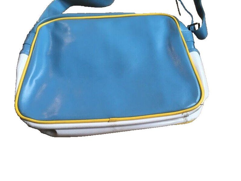May include: A blue, white, and yellow shoulder bag. The bag has a rectangular shape with a light blue center, white sides, and yellow trim. The strap is blue.