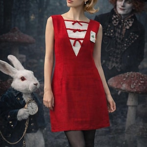 Könnte beinhalten: Ein rotes ärmelloses Kleid mit weißem Lätzchen-Design und Schleifenakzenten. Eine Spielkarte ist an dem Kleid befestigt. Das Bild hat ein skurriles Thema, mit einem weißen Kaninchen, das eine Taschenuhr hält, und einem Mann mit Zylinder im Hintergrund.